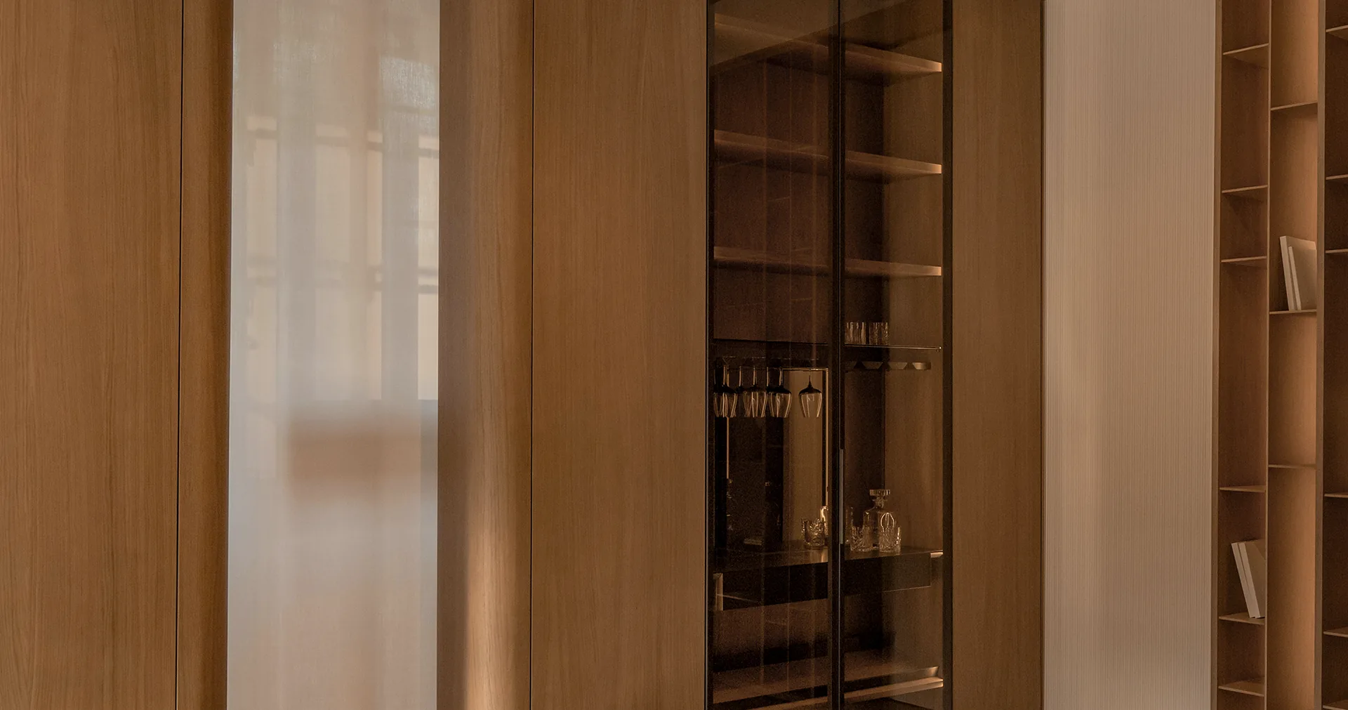 Timber living-room cabinetry combining a glazed bar, concealed doors and illuminated shelving