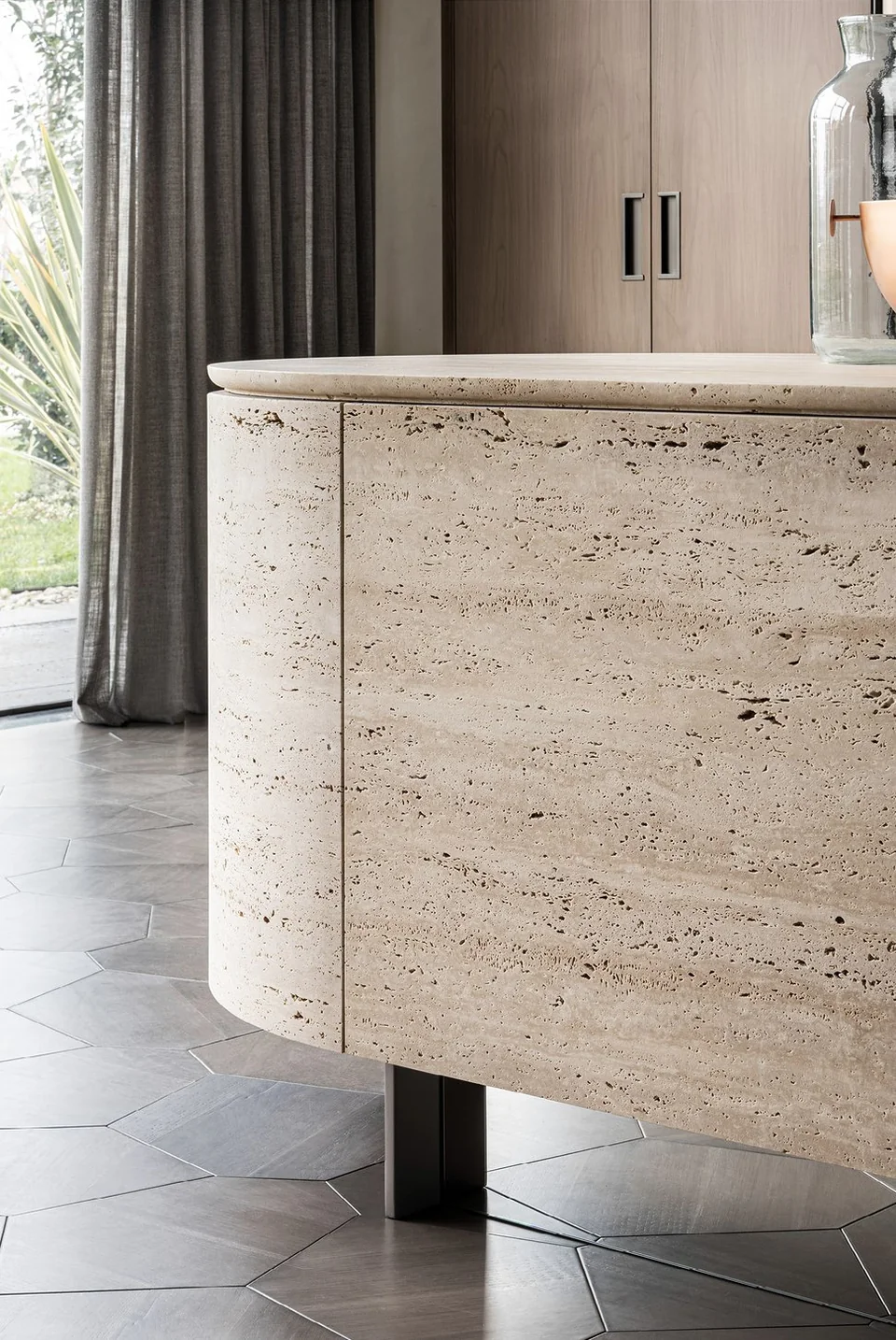 Close view of the curved travertine island, with a continuous stone edge and timber cabinetry beyond