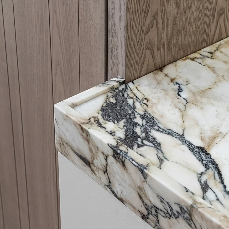 Veined stone worktop meeting vertically grained timber cabinetry
