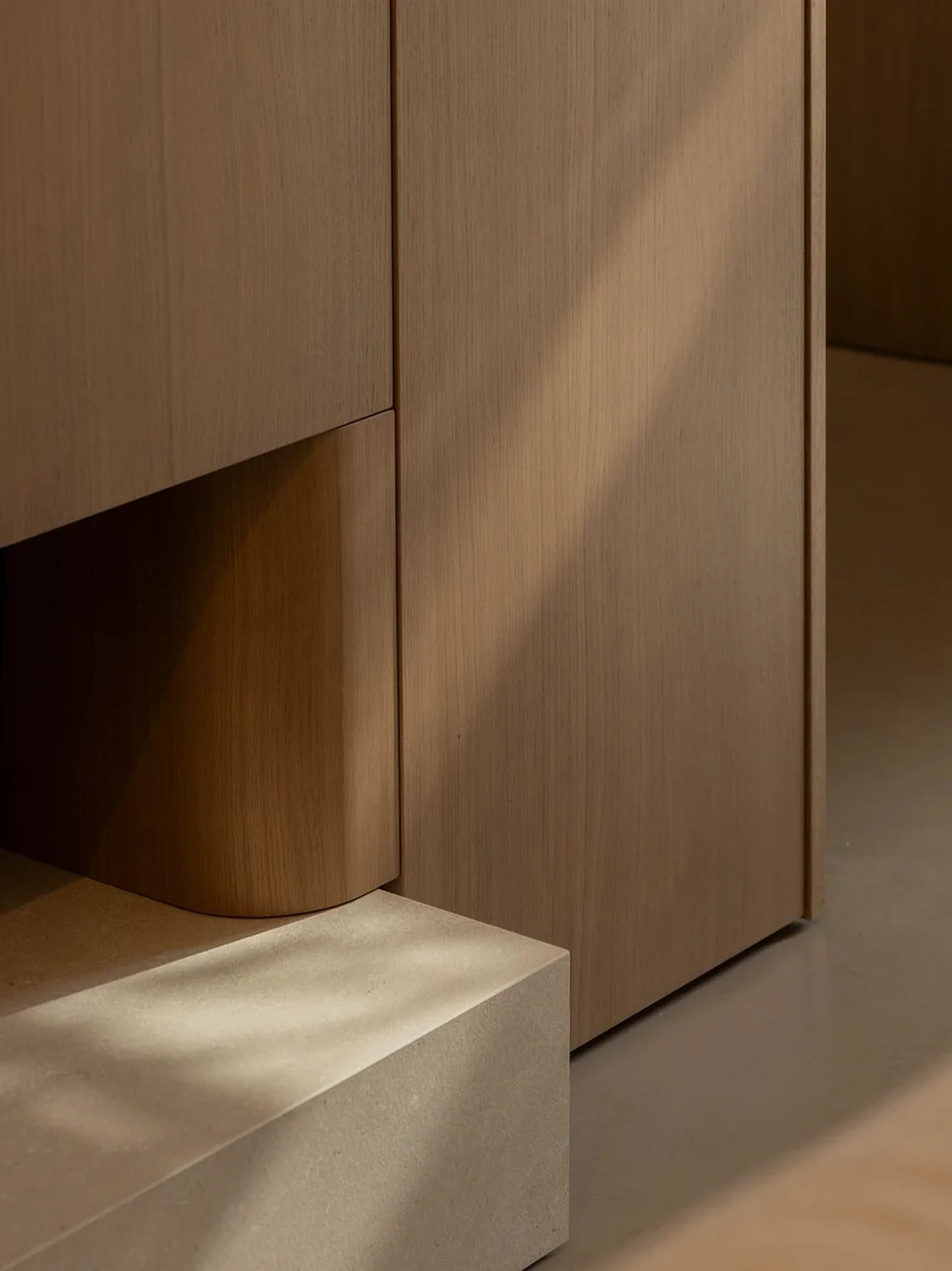 Curved timber panel meeting a stone ledge beside concealed cabinetry